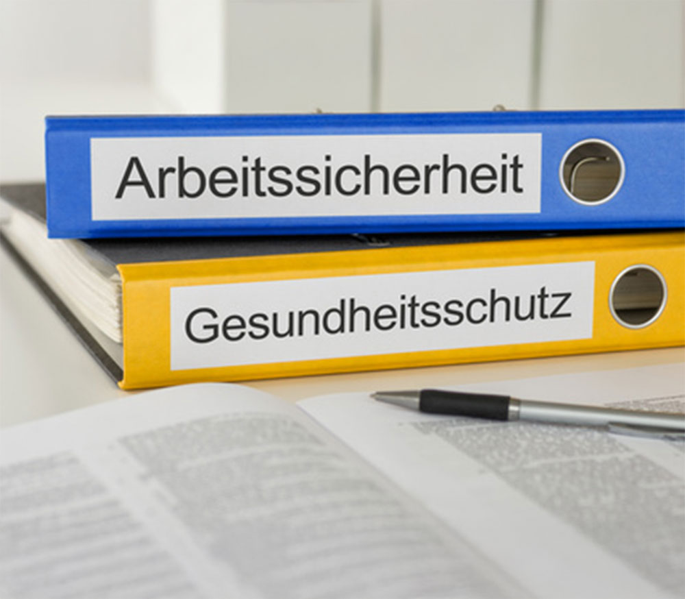 Zwei Büroordner mit Aufschrift Arbeitssicherheit und Gesundheitsschutz liegen auf einem Tisch
