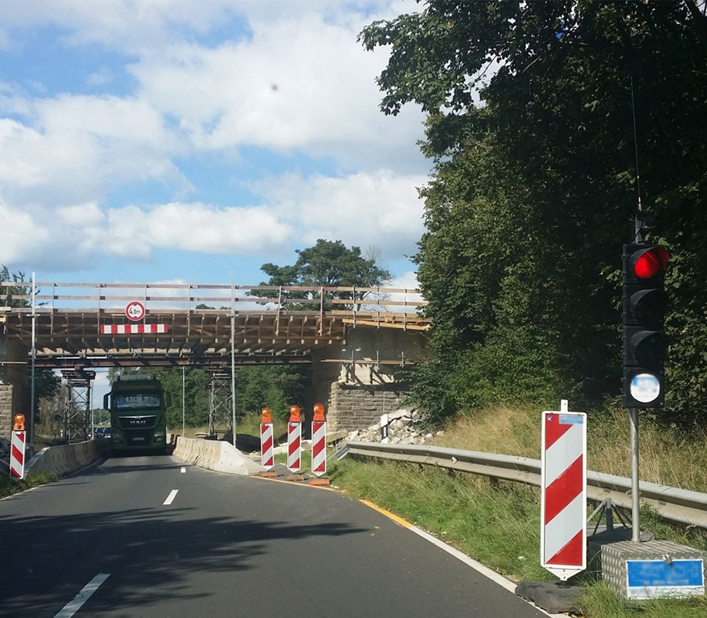 Schulung Temporäre (transportable) Lichtzeichenanlagen LKW fährt unter einer Brücke durch eine Baustelle mit Lichtzeichenanlage, welche rot leuchtet.