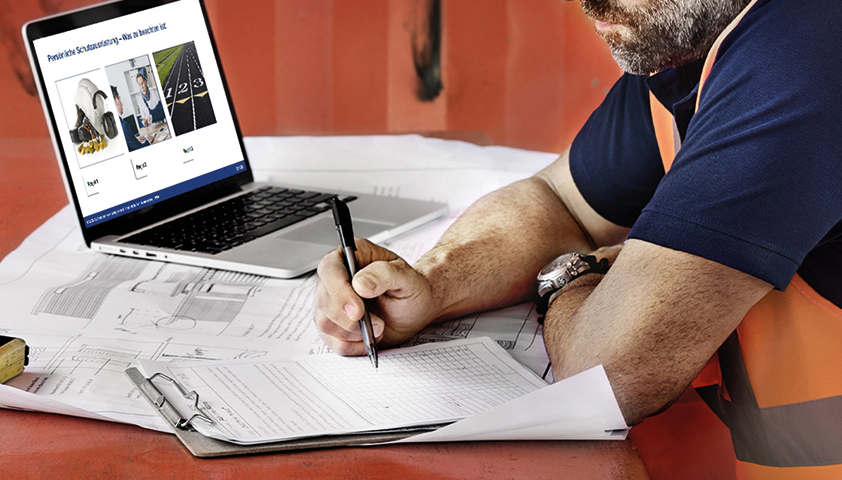 Mann am Laptop notiert etwas auf einem Zettel am Klemmbrett