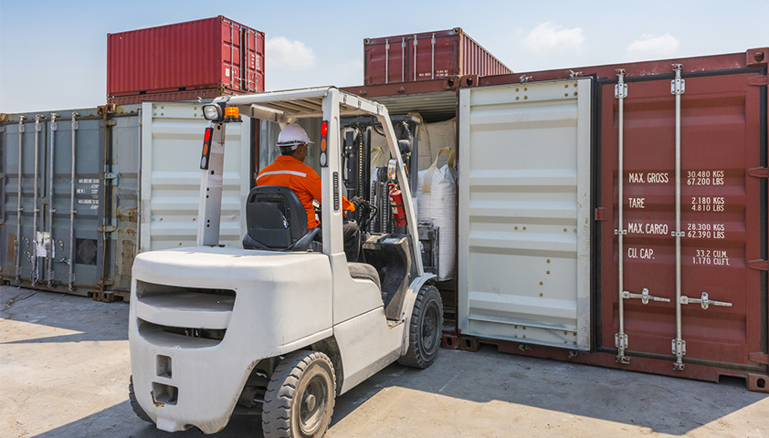 MORAVIA Akademie Aktuell: Fahrausweis-Schulungen nach Bedarf Arbeiter bedient einen Gabelstapler und lädt Waren in einen Schiffscontainer in einer Hafenanlage.