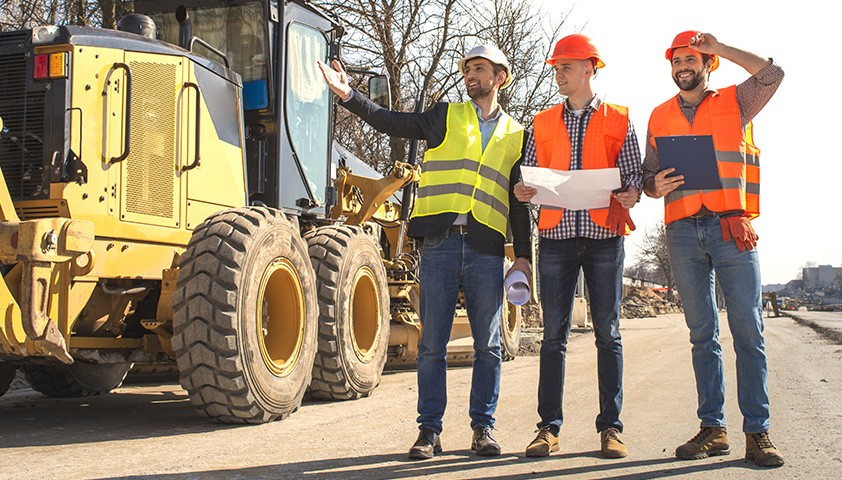 MORAVIA Akademie Aktuell: Digitaler Kurs zur Verkehrssicherung & aktuelle Änderungen im Straßenverkehrsgesetz Bauarbeiter in Sicherheitswesten und Helmen besprechen Pläne auf einer Baustelle, im Hintergrund schwere Maschinen.
