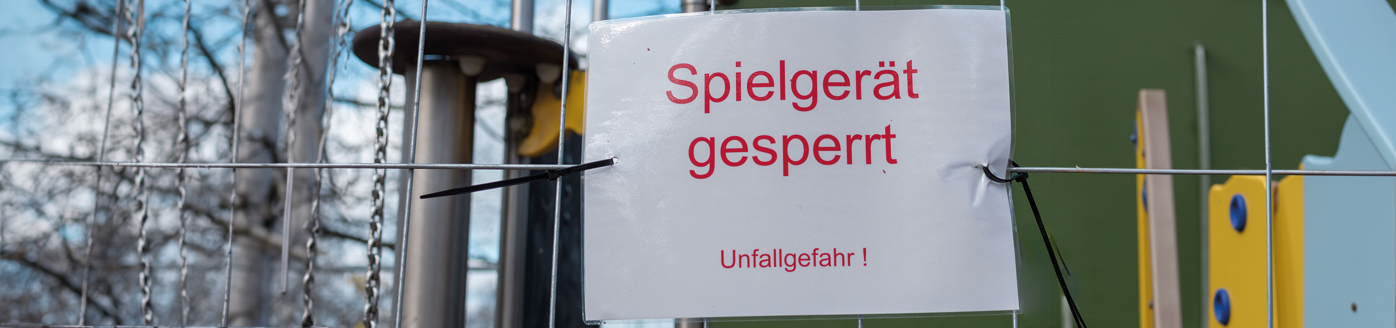 Sicherheit geht vor: Warum qualifizierte Spielplatzprüfer unverzichtbar sind Ein Schild "Spielgeräte gesperrt Unfallgefahr" hängt an einem Drahtzaun bei einem Spielplatz.