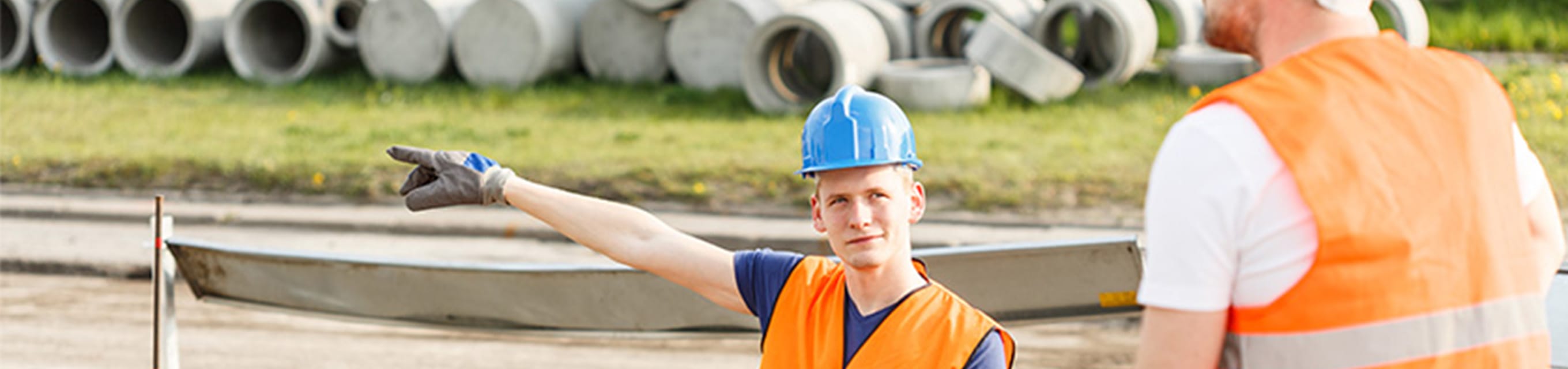 Weiterer Durchgang Oktober 2024 Zertifikatslehrgang Straßenbau und Straßenerhaltung Zwei Bauarbeiter auf einer Baustelle, der Man mit dem blauen Helm zeigt in eine Richtung.