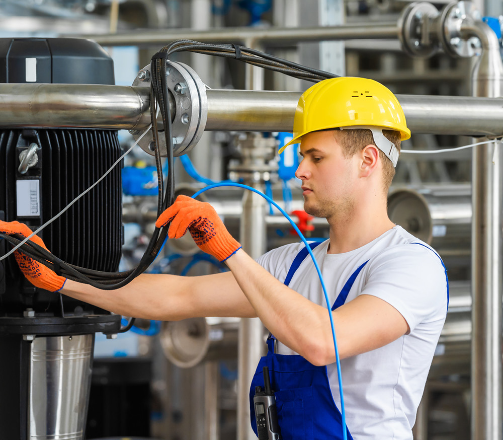 Jährliche Unterweisung für Elektrotechnisch unterwiesene Person (EuP) und Elektrofachkraft für festgelegte Tätigkeiten (EffT) Ein Mann in einem industriellen Umfeld bedient eine Maschine und trägt dabei Schutzkleidung.